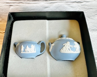 May include: A blue and white porcelain creamer and sugar bowl set with a white floral design. The set is in a black box with white foam padding.