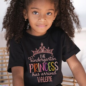 May include: A black t-shirt with a pink crown and the text "The kindergarten princess has arrived Valerie" in rainbow colours.