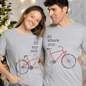 Puede incluir: Una pareja lleva camisetas grises a juego con un gráfico de bicicleta roja. La camiseta de la mujer dice "I'd go any with" y la camiseta del hombre dice "go where you".