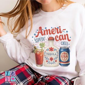 Puede incluir: Sudadera blanca con el texto "American Sippin' Chill" en rojo y azul. El gráfico incluye un cóctel, una botella de tequila y una lata con "USA". La sudadera se usa con pantalones de cuadros rojos y azules.