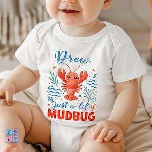 May include: White baby bodysuit with a red lobster graphic and the text "Drew just a lil MUDBUG". The design includes blue waves, green seaweed, and orange stars. The bodysuit is short-sleeved.