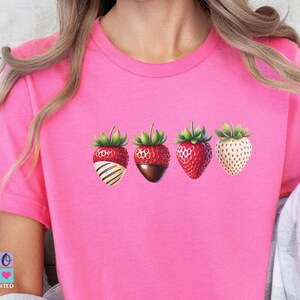 Puede incluir: Camiseta rosa con un gráfico de cuatro fresas bañadas en chocolate. Las fresas están dispuestas en una fila, con las fresas cubiertas de chocolate a la izquierda y las fresas normales a la derecha.