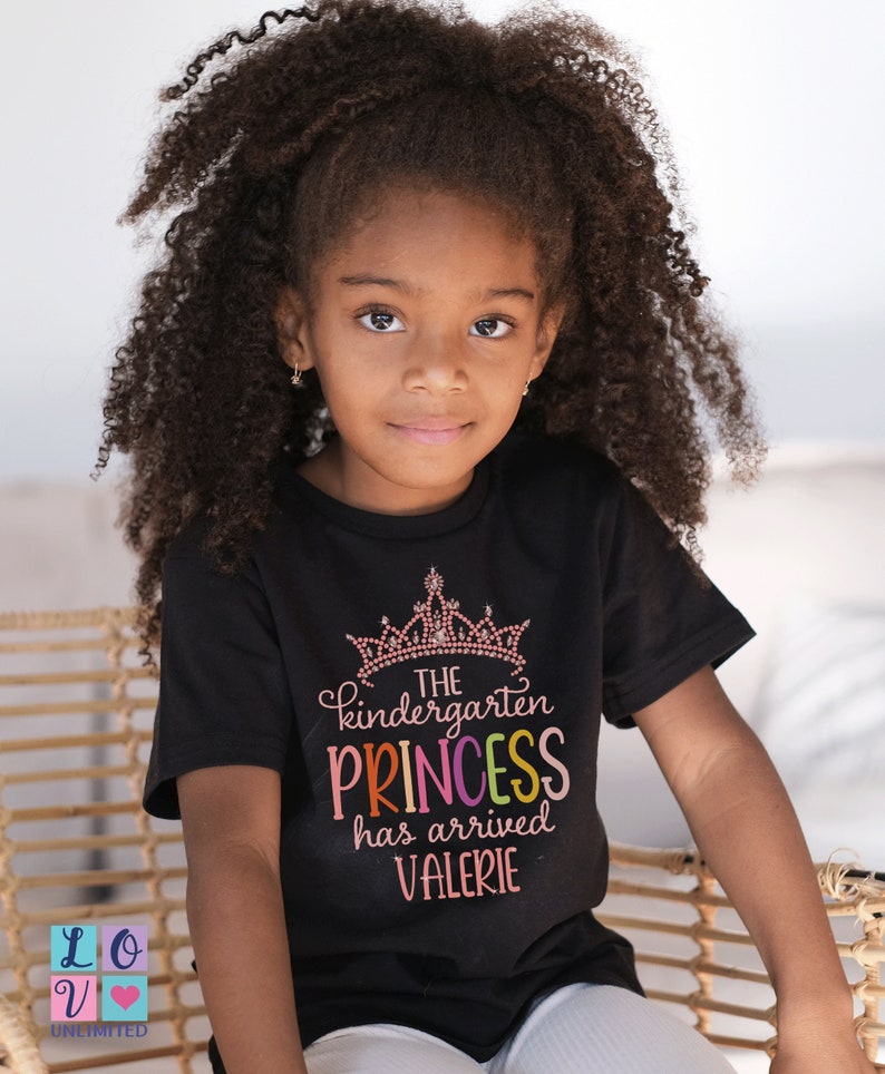 May include: A black t-shirt with a pink crown and the text "The kindergarten princess has arrived Valerie" in rainbow colours.