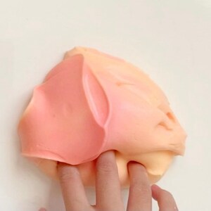 May include: A close-up of a pink and orange slime being stretched and pulled by a finger.