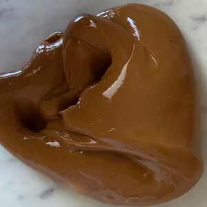 Puede incluir: Primer plano de una slime lisa, marr&oacute;n, de color chocolate. La slime est&aacute; en un bol y tiene un acabado brillante.