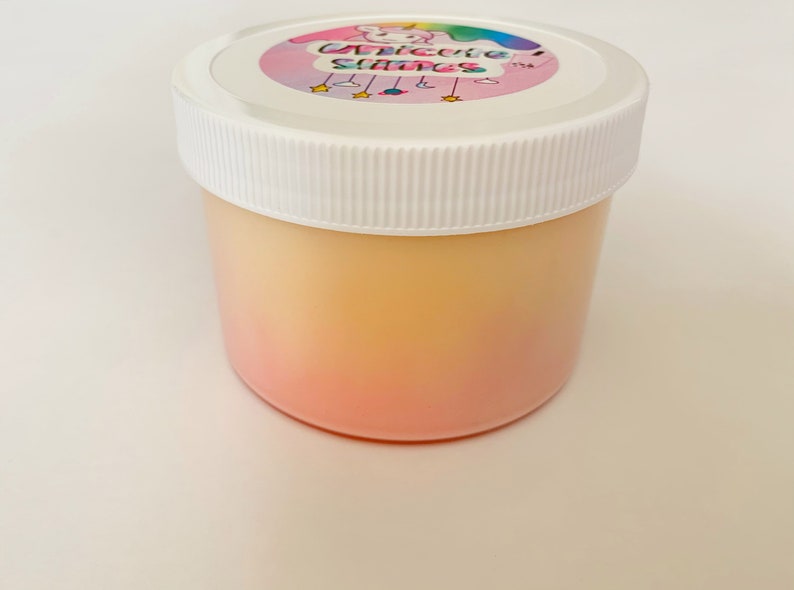 May include: A clear plastic jar with a white lid. The jar contains a pink and yellow ombre slime. The lid has a sticker with a cartoon unicorn and the text "Unicorns Slime".