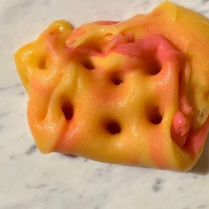 Può includere: Primo piano di un giocattolo di slime colorato. Lo slime è un mix di giallo, arancione e rosa, con una superficie strutturata e diversi fori. Il giocattolo è probabilmente per bambini ed è un'attività sensoriale popolare.