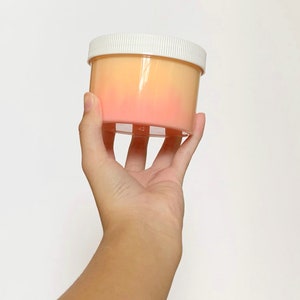 May include: A clear plastic container with a white lid filled with a pink and orange slime.