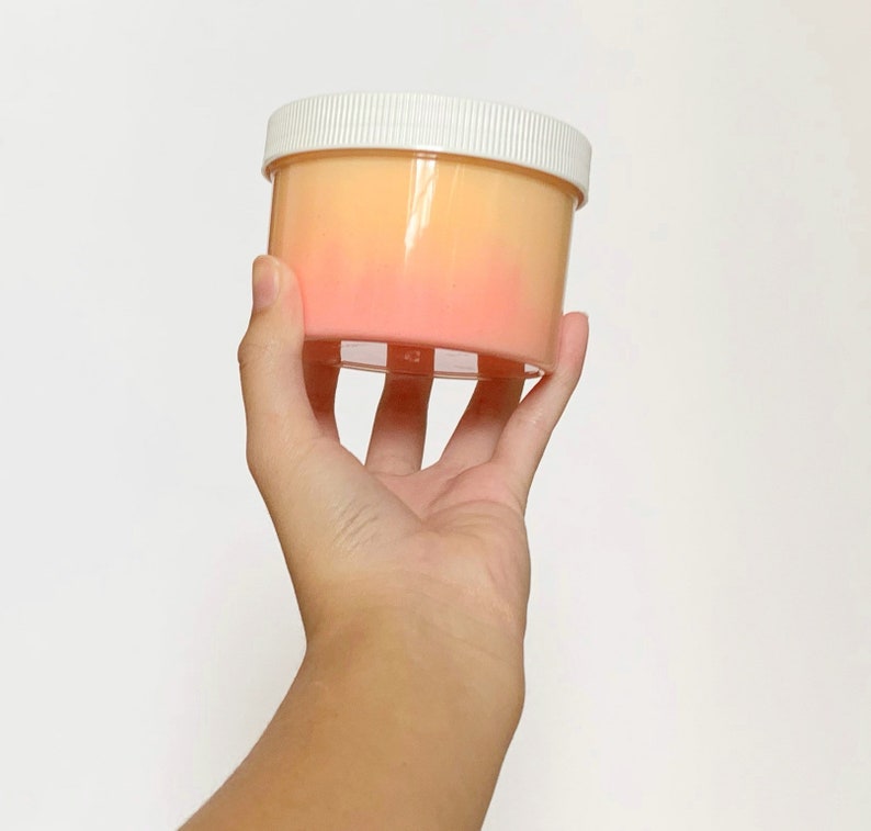 May include: A clear plastic container with a white lid filled with a pink and orange slime.