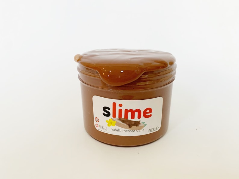Puede incluir: Una slime marr&oacute;n en un tarro transparente con una etiqueta blanca que dice "slime" en letras rojas y "nutella themed slime" en letras negras.