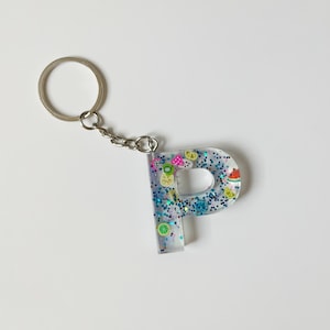 May include: A clear resin keychain with a blue glitter background and colorful fruit charms in the shape of the letter "P".