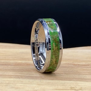 May include: A silver ring with a green and brown inlay. The ring is on a wooden surface.
