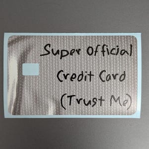 May include: A rectangular sticker with a light gray textured background featuring the handwritten black text Super Official Credit Card (Trust Me) and a small white square on the left side. The sticker has a thin white border around the edge.