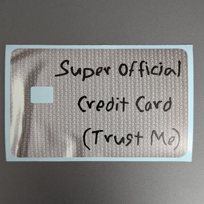 May include: A rectangular sticker with a light gray textured background featuring the handwritten black text Super Official Credit Card (Trust Me) and a small white square on the left side. The sticker has a thin white border around the edge.