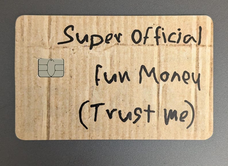 May include: A rectangular card made of corrugated cardboard with rounded corners. The card has the words "Super Official fun Money (Trust me)" written in black marker. A silver SIM card is on the left side.
