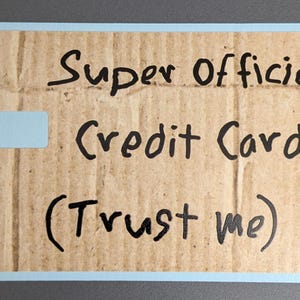 May include: A rectangular card with a light blue border and a cardboard-like texture. The text "Super Official Credit Card (Trust me)" is handwritten in black. A small, light blue rectangle is in the upper left corner.