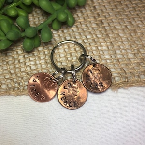 May include: A keychain with three copper pennies, each engraved with a name: "Jayce", "Andace", and "Aelan". The pennies are attached to a silver key ring.