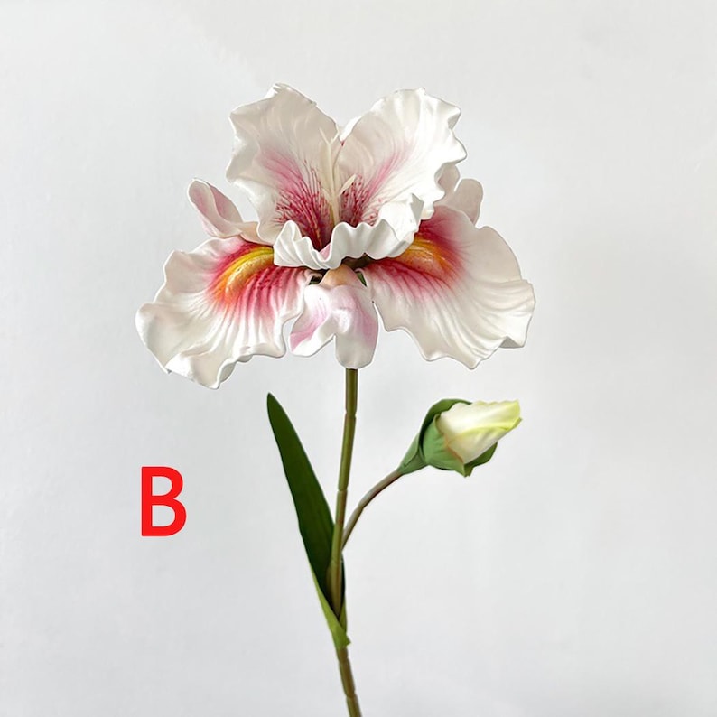 May include: A single white and pink artificial iris flower with a yellow center and a green stem. The flower has a bud on the stem. The flower is on a white background.