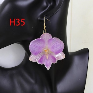 May include: A dangling earring featuring a large, realistic purple orchid flower petal design with a glossy finish. The earring is attached to a gold-toned metal hook. The text H35 is visible in red in the upper left corner of the image.