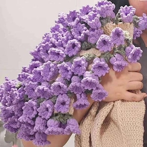 May include: A crocheted purple flower garland with green stems. The garland is made of individual crocheted flowers that resemble bells.