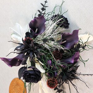 May include: A dramatic floral bouquet with deep purple calla lilies, black roses, and white accents. The arrangement incorporates various textures and shades of green, with a touch of white ribbon.