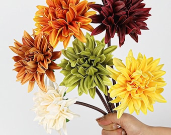 May include: A bouquet of artificial dahlia flowers in various colors, including orange, burgundy, yellow, green, and cream. The flowers are held together by brown stems, creating a vibrant and colorful arrangement.