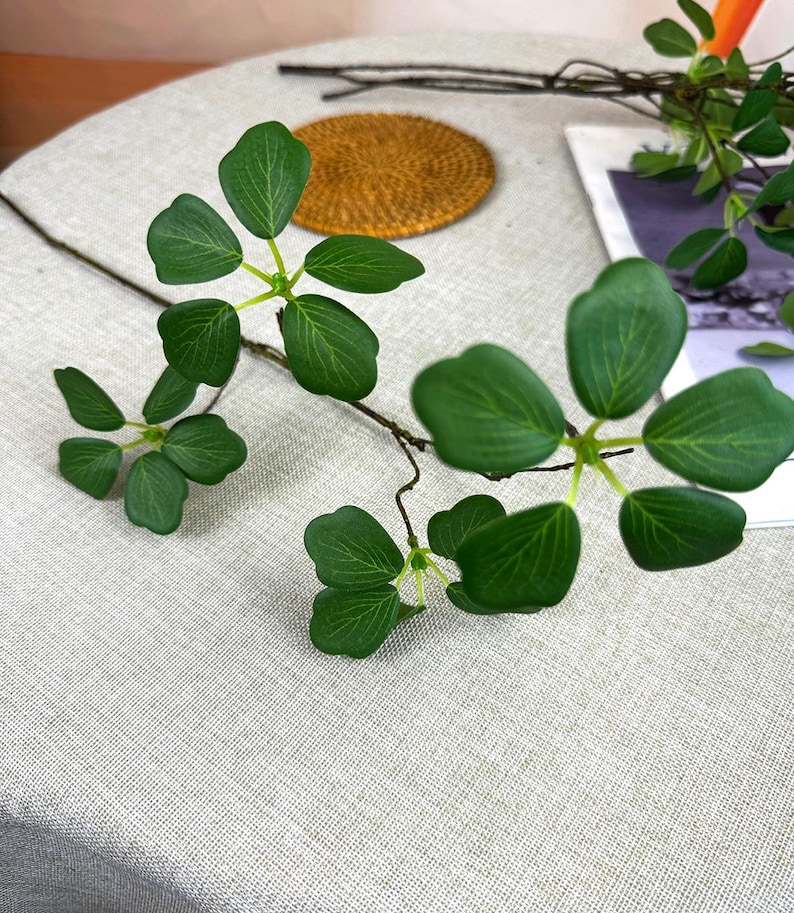 Pu&ograve; includere: Steli di foglie verdi artificiali con pi&ugrave; foglie. Le foglie sono di un verde vibrante con venature dettagliate. I gambi sono marroni e sembrano essere fatti di un materiale flessibile. Le foglie sono disposte in un motivo naturale e organico.