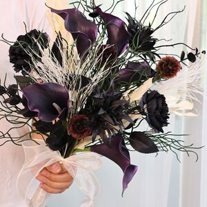 May include: A striking bouquet with deep purple calla lilies, black roses, and burgundy and white accents. The arrangement includes delicate branches and is tied with an ivory ribbon. A sophisticated floral design, perfect for a special occasion.