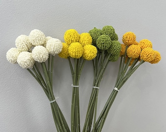 May include: A bouquet of artificial flowers with white, yellow, and green flower heads. The stems are green and bundled together.