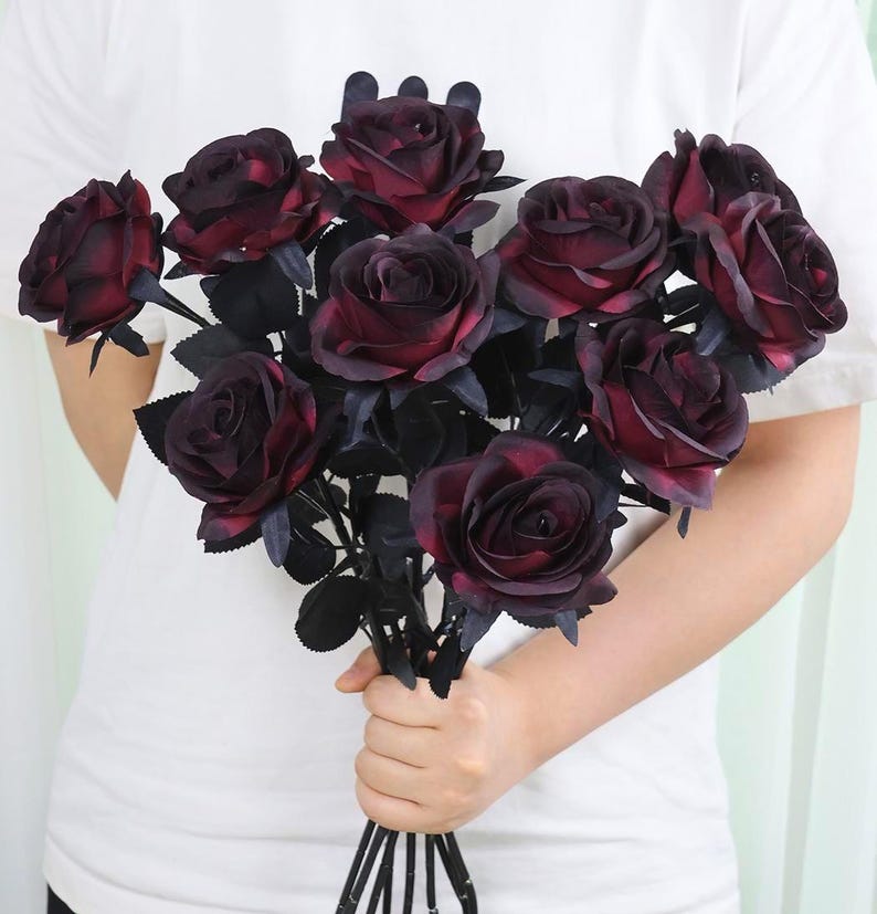 May include: A bouquet of dark red roses with black stems and leaves. The roses have a velvety texture and are in full bloom, creating a dramatic and elegant floral arrangement.