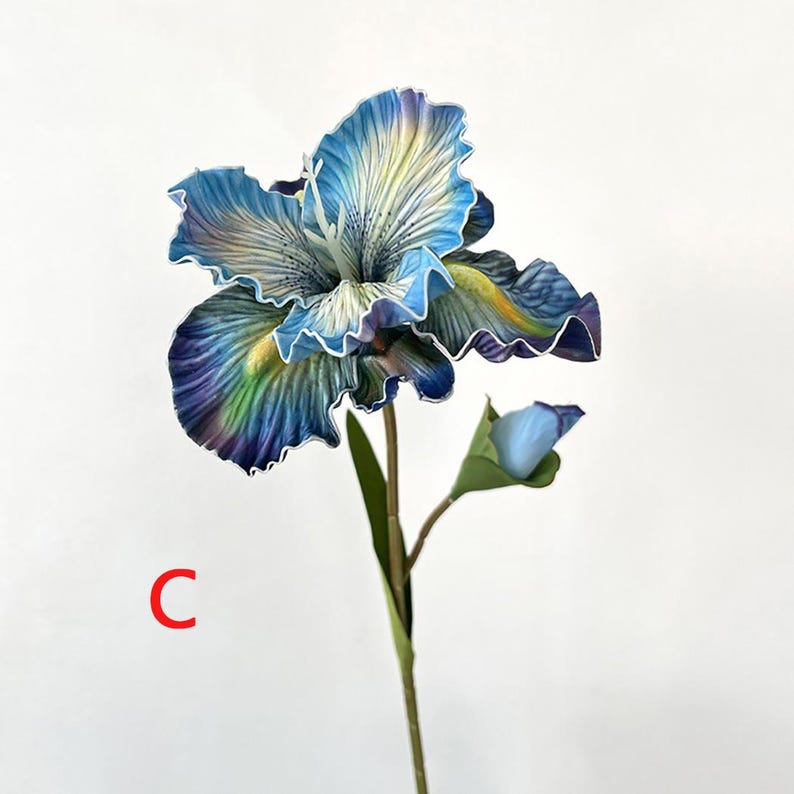 May include: A single artificial blue and green iris flower with a bud on a green stem. The flower has a white center and a ruffled edge.