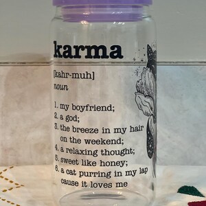 May include: A clear glass jar with a purple lid and a black and white illustration of a cat. The jar has the word "karma" printed on it in black letters, along with the definition: "[kahr-muh] noun 1. my boyfriend; 2. a god; 3. the breeze in my hair on the weekend; 4. a relaxing thought; 5. sweet like honey; 6. a cat purring in my lap cause it loves me"