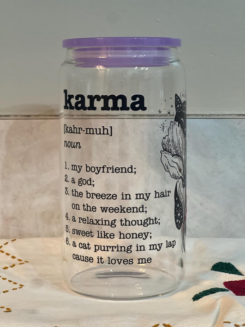 May include: A clear glass jar with a purple lid and a black and white illustration of a cat. The jar has the word "karma" printed on it in black letters, along with the definition: "[kahr-muh] noun 1. my boyfriend; 2. a god; 3. the breeze in my hair on the weekend; 4. a relaxing thought; 5. sweet like honey; 6. a cat purring in my lap cause it loves me"