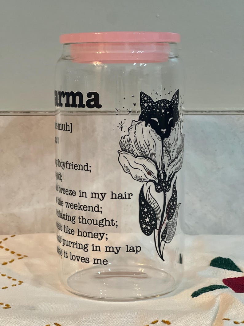 May include: A clear glass jar with a pink lid and a black and white illustration of a cat in a flower. The text on the jar reads "arma [muh] boyfriend; breeze in my hair the weekend; relaxing thought; sweet like honey; cat purring in my lap cause it loves me".