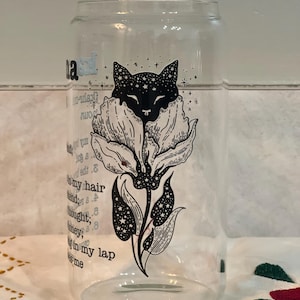 May include: A clear glass cup with a black and white illustration of a cat with stars in its fur, inside a flower. The text "Sleep in my hair, friend; thought, honey; Sleep in my lap, me" is printed on the cup.