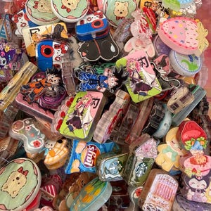 Könnte beinhalten: Eine Sammlung bunter Resin-Anhänger mit verschiedenen Designs. Die Anhänger zeigen Zeichentrickfiguren, Lebensmittel und andere dekorative Elemente. Einige Anhänger ähneln Kameras, Erdbeeren und Starbucks-Tassen. Die Farbpalette ist lebendig, mit Rosa, Blau und Grün.