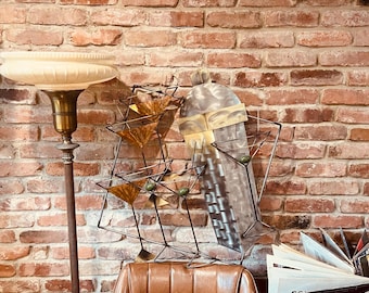 May include: A vintage-style bar display featuring a metal martini glass rack with three glasses, a cocktail shaker, and a leather chair. The background is a brick wall, and a floor lamp is visible on the left.