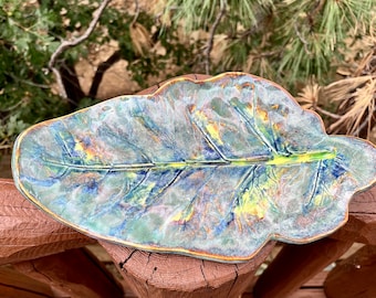 May include: A ceramic leaf-shaped serving dish with a blue, green, and yellow glaze. The dish has a realistic leaf texture and is perfect for serving snacks or appetizers.