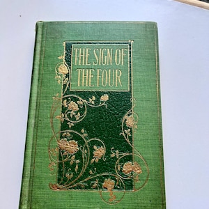 May include: A green hardcover book with gold lettering on the spine and front cover. The title of the book is "The Sign of the Four".