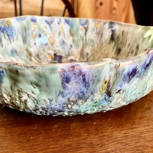 May include: A large, ceramic bowl with a wavy rim. The bowl is decorated with a colorful glaze in shades of blue, green, purple, and yellow.