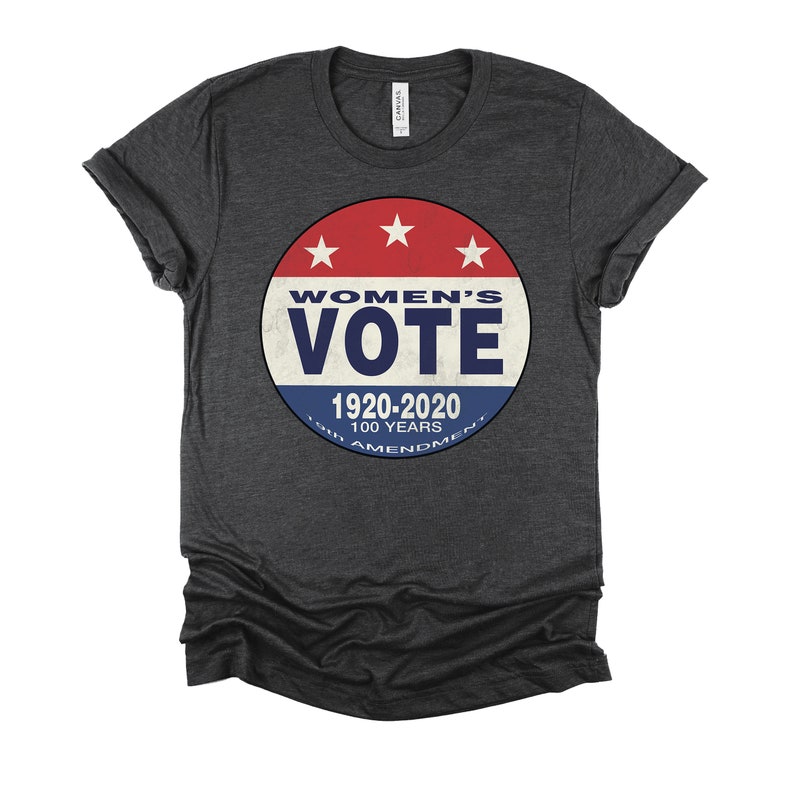 May include: A dark gray t-shirt with a red, white, and blue circular graphic that says "Women's Vote" with the text "1920-2020 100 Years 19th Amendment" underneath.