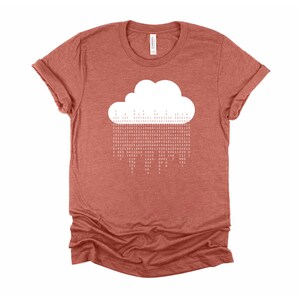 Op de afbeelding: Een roestkleurig T-shirt met een witte wolk-afbeelding. De wolk is gemaakt van een reeks binaire code.