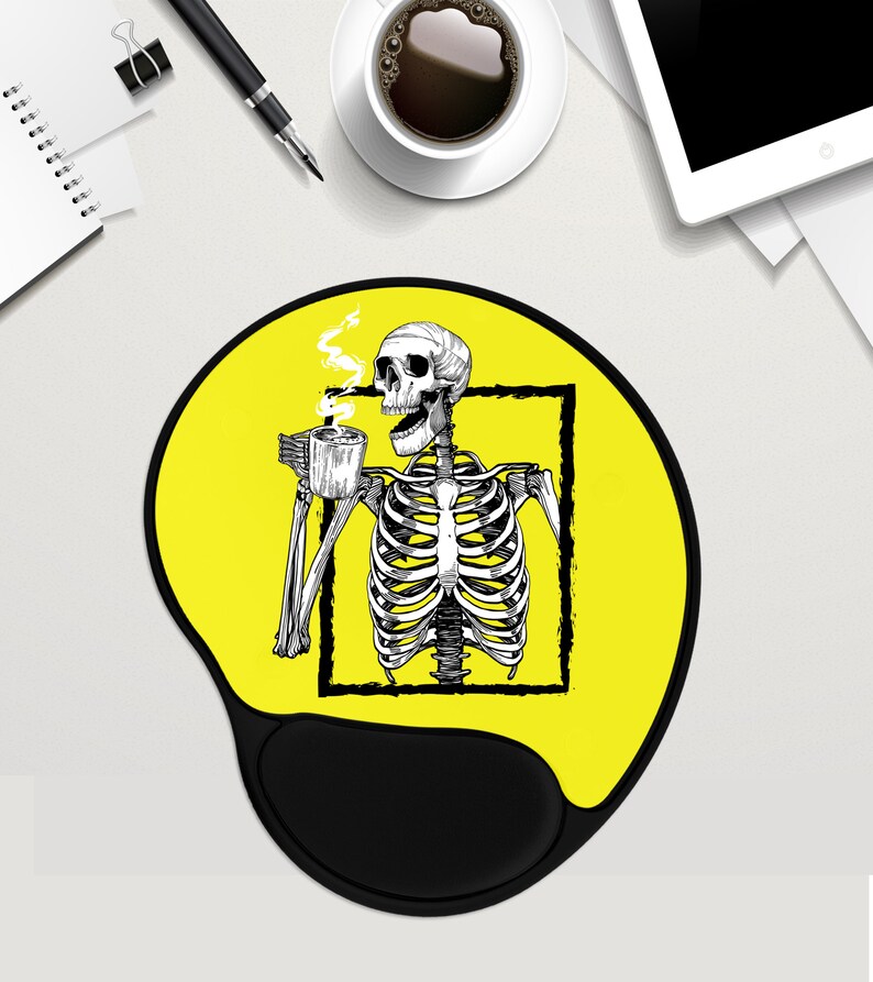 May include: A yellow mouse mat with a black skeleton drinking coffee. The skeleton is inside a black square frame. The mouse mat has a black wrist rest.