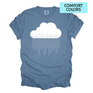Pode incluir: Camiseta azul com um desenho de nuvem branca e c&oacute;digo bin&aacute;rio representando a chuva. O texto "COMFORT COLORS" est&aacute; em uma caixa azul clara no canto superior direito. Gola redonda e mangas curtas.