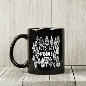 May include: Black ceramic coffee mug with a white design of arrowheads and the text "Let's get to the point".