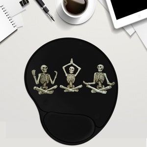 May include: Black mouse pad with three skeletons in yoga poses. The skeletons are white with black outlines and are in different yoga poses. The mouse pad is black and has a raised edge.