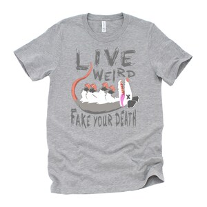 Op de afbeelding: Grijs T-shirt met een cartoon opossum en de tekst "Live Weird Fake Your Death".