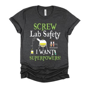 May include: Dark gray t-shirt with green text that reads "SCREW Lab Safety I WANT SUPERPOWERS!"  The shirt features a cartoon illustration of a beaker and test tubes.