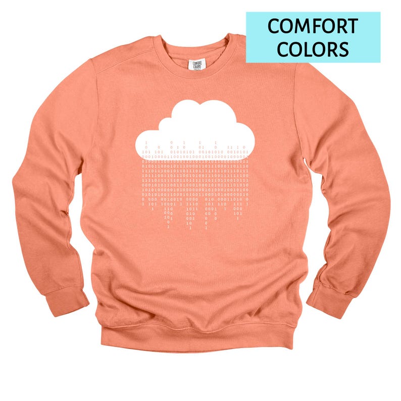 Op de afbeelding: Koraalrood sweatshirt met een witte wolkengrafiek en binaire code regen. De tekst "COMFORT COLORS" staat in een lichtblauwe rechthoek. De sweatshirt heeft lange mouwen en een ronde hals.