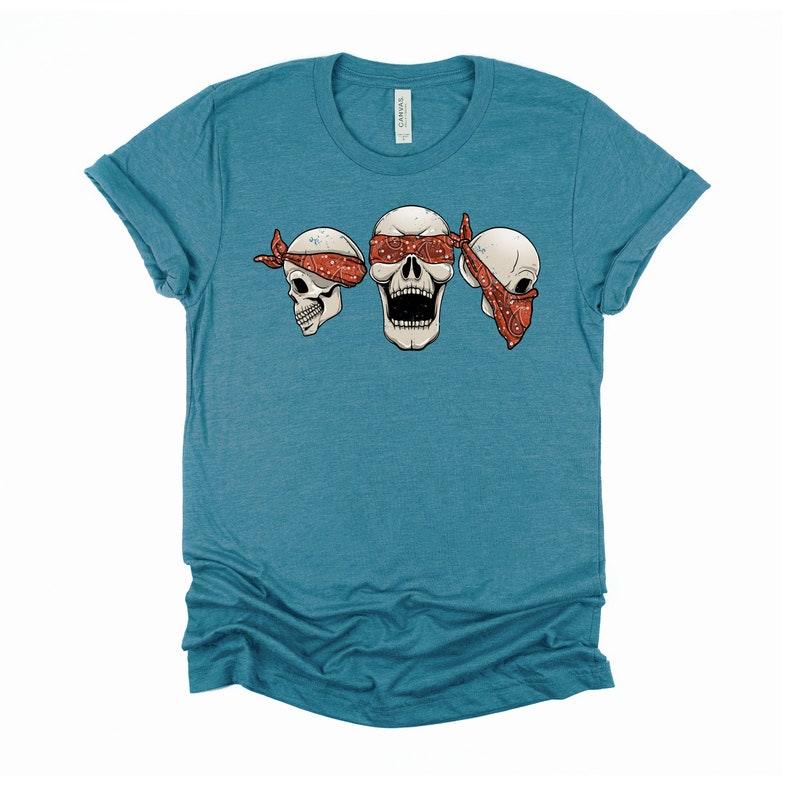 May include: A teal blue t-shirt with three white skulls wearing red bandanas. The skull in the middle has its eyes covered by the bandana.